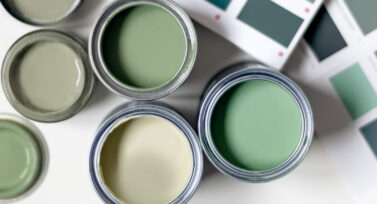 Tiny sample paint cans during house renovation, process of choosing paint for the walls, different green colors, color charts on background